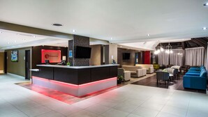 A modern hotel lobby with a reception desk, seating area, and a large chandelier. - Ramada by Wyndham Jacksons Point (Georgina)