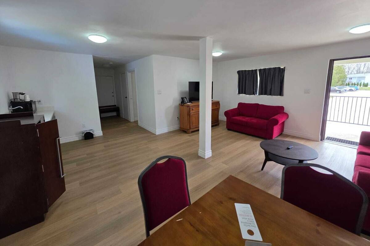A room with a wooden dining table, red chairs, a red sofa, a TV, and a wooden cabinet.