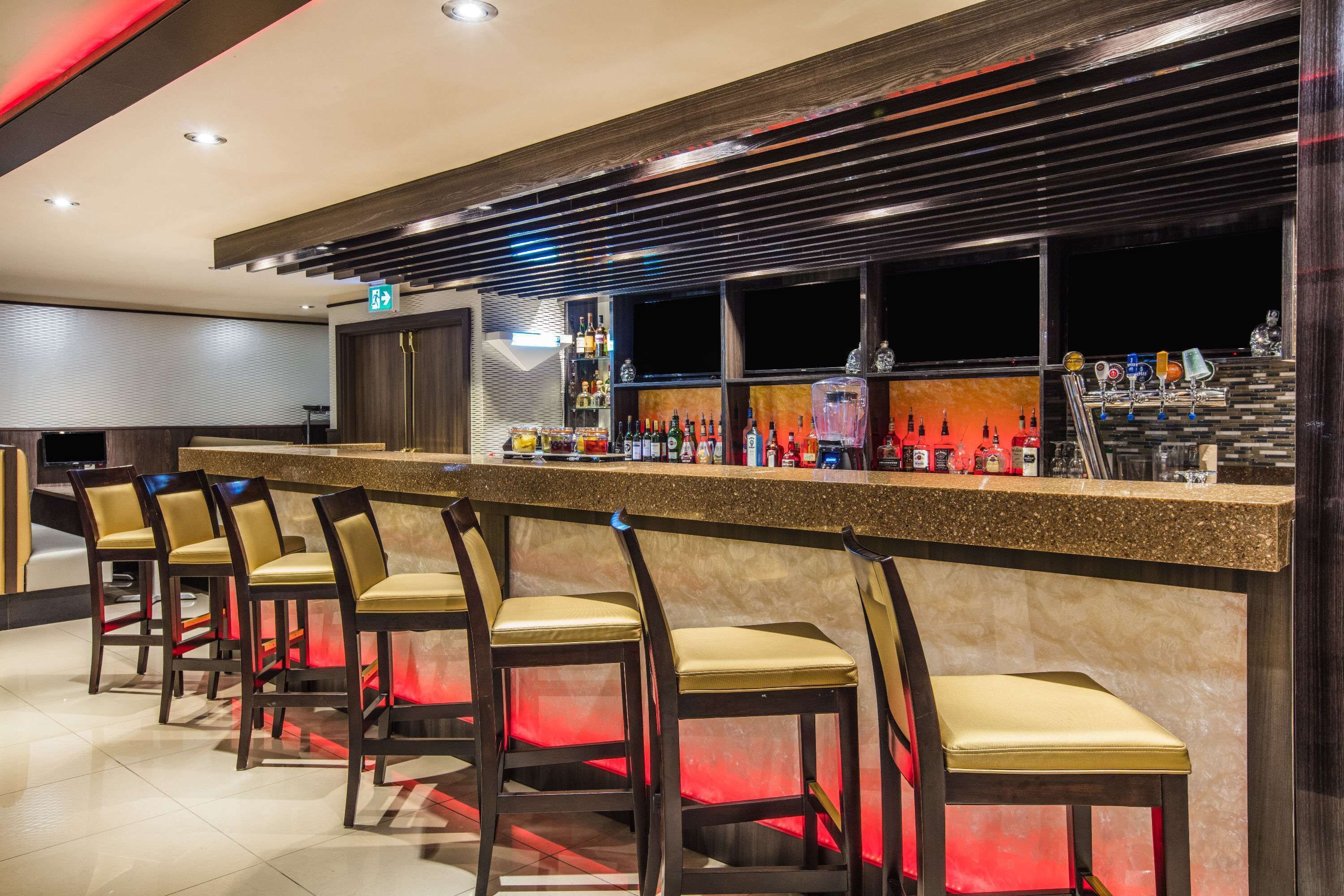 A bar area with a long counter, multiple stools, and a variety of bottles and glasses.