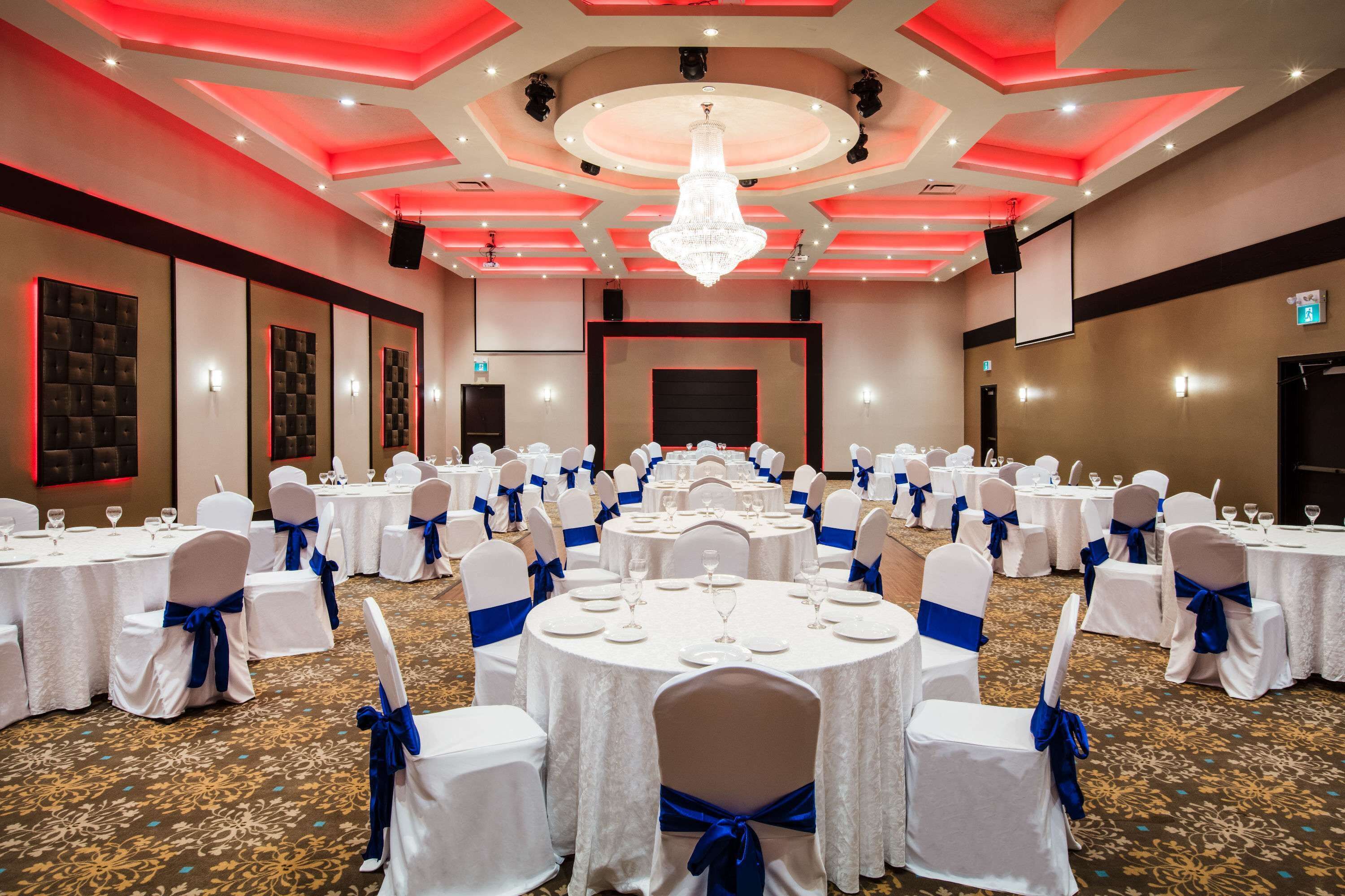 A banquet hall with round tables, white chairs with blue sashes, and a chandelier.