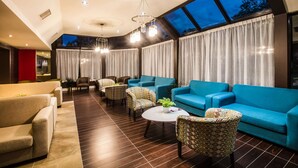 A modern living room with a high ceiling, large windows, and a variety of seating options including sofas and patterned chairs. - Ramada by Wyndham Jacksons Point (Georgina)