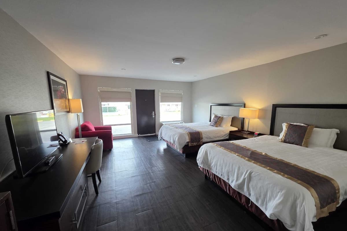 A hotel room with two beds, a desk with a TV, and a red chair.