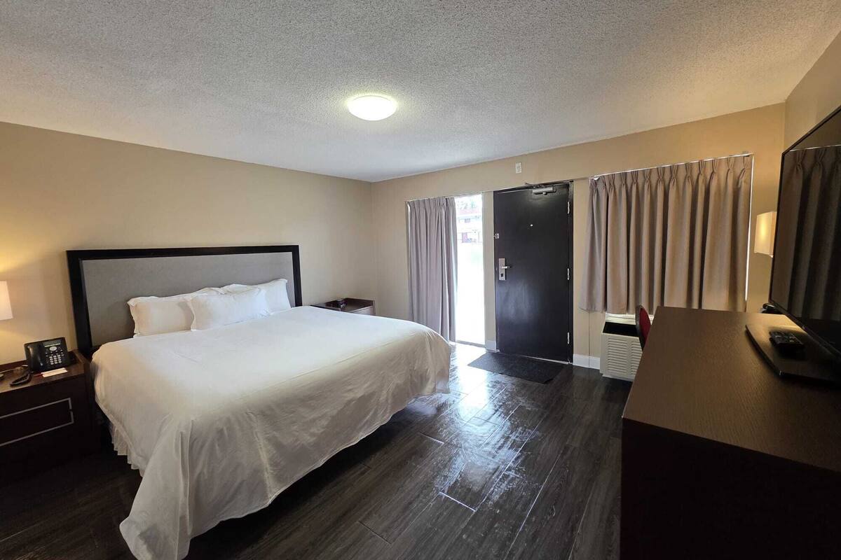 A hotel room with a large bed, a desk with a chair, a telephone, and a door leading to another room.
