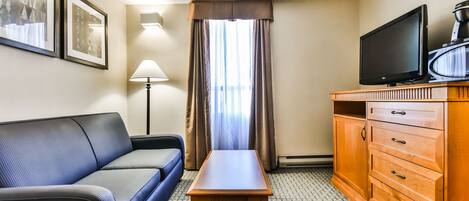 A hotel room with a sofa, a small table, a wooden cabinet with drawers, a television, and framed pictures on the wall.