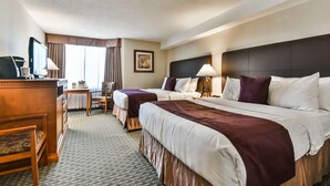 Una habitación de hotel con dos camas, un escritorio con computadora, una silla y una ventana con cortinas.
