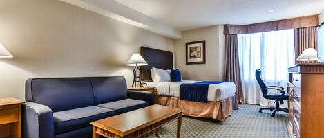 A hotel room with a bed, a sofa, a desk, and a chair.