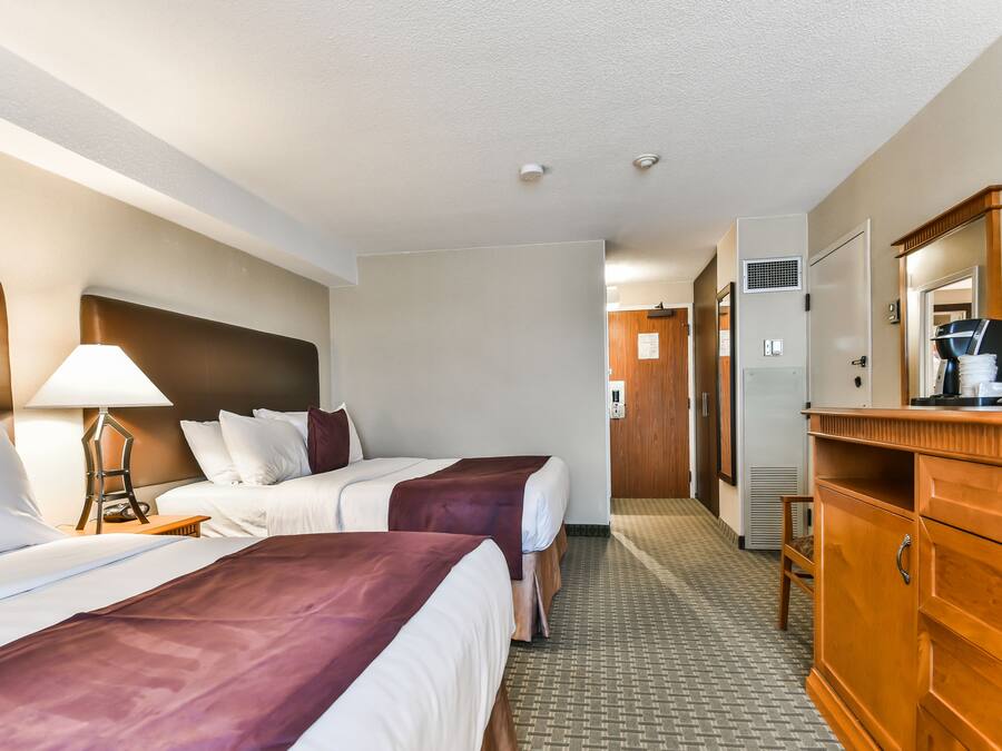 Ein Hotelzimmer mit zwei Betten, einem Holzkonsolentisch, einer Lampe und einem Flur, der zu einer Tür führt.