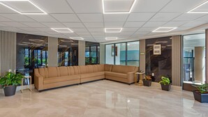A modern lobby with a beige sectional sofa, potted plants, and a glass wall offering a view of the outdoors. - Quality Inn & Suites (Brampton)