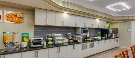 Una cocina moderna con armarios blancos, un microondas y una cafetera. Hay recipientes con comida en la encimera y un cartel que dice "healthy".