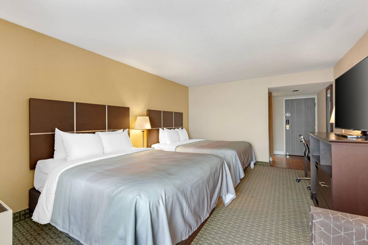 A hotel room with two beds, a desk with a flat-screen TV, and a wardrobe.