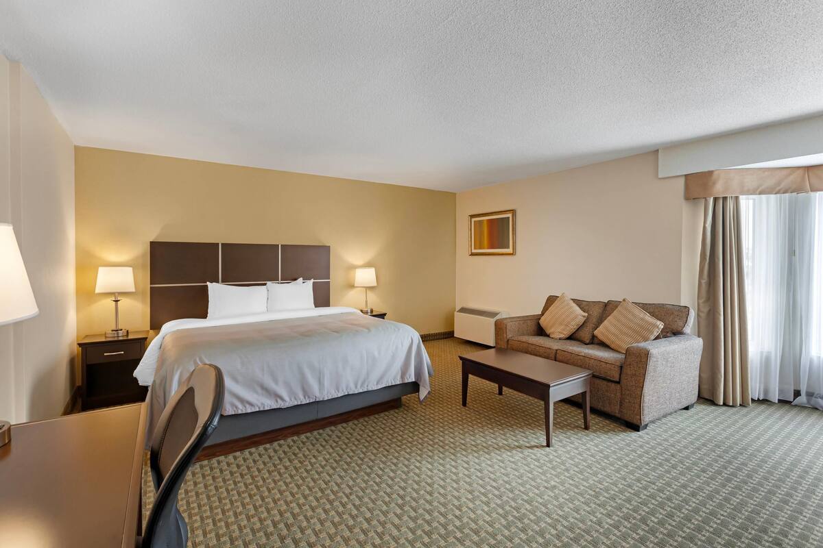 A hotel room with a bed, a sofa, a coffee table, and a desk.
