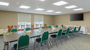 A conference room with a long table, green chairs, water bottles, and a TV screen on the wall.