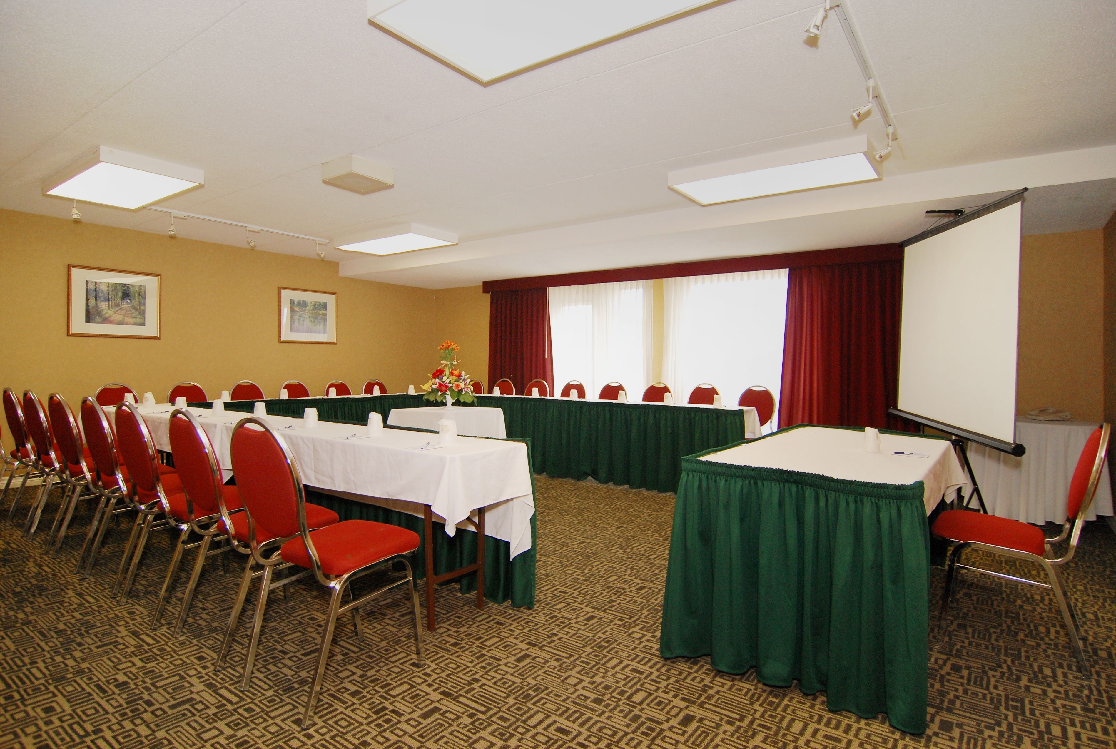 A conference room with rows of red chairs, white tables, and a projector screen.