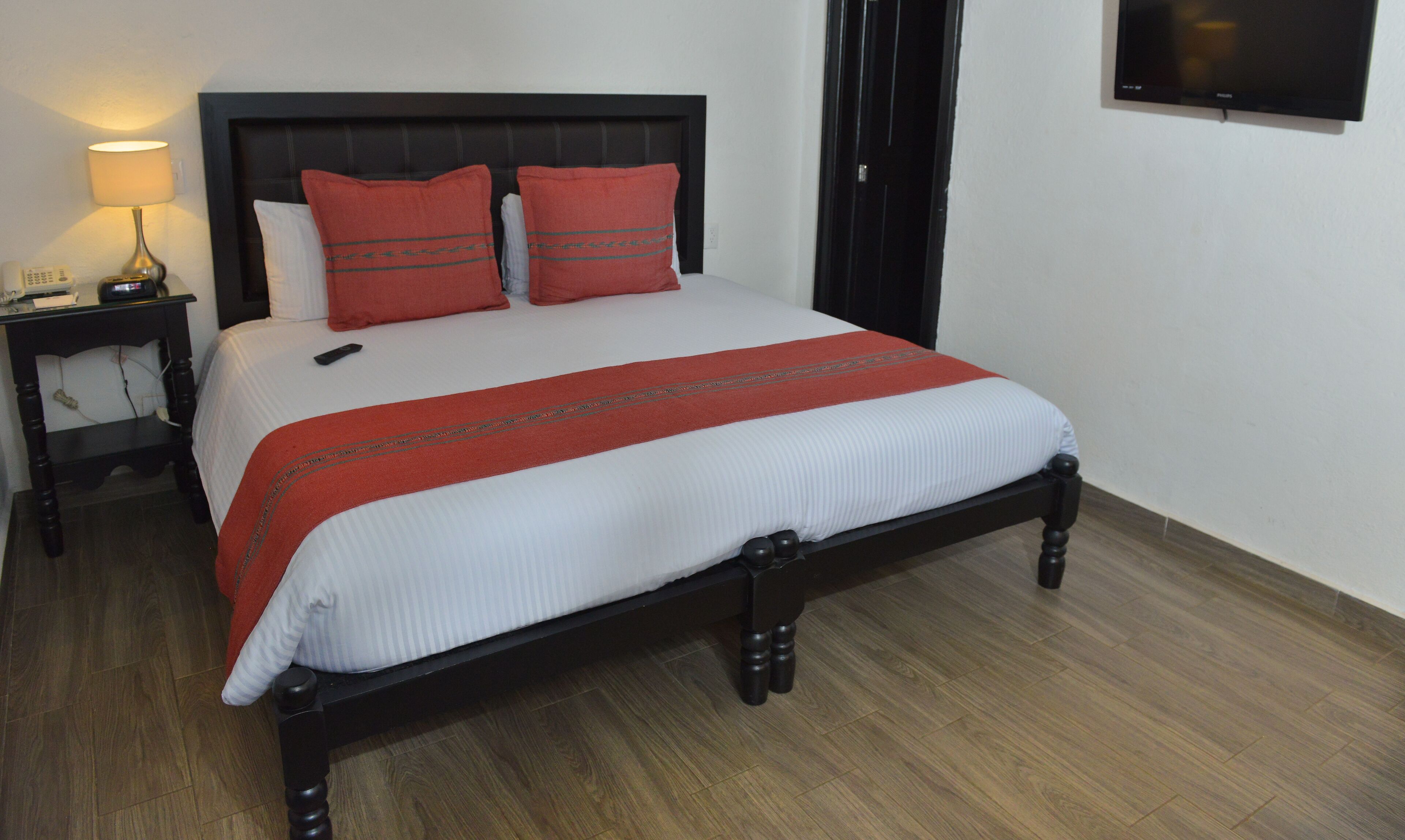 Una cama bien hecha con una colcha roja y blanca, un cabecero negro y un piso de madera.