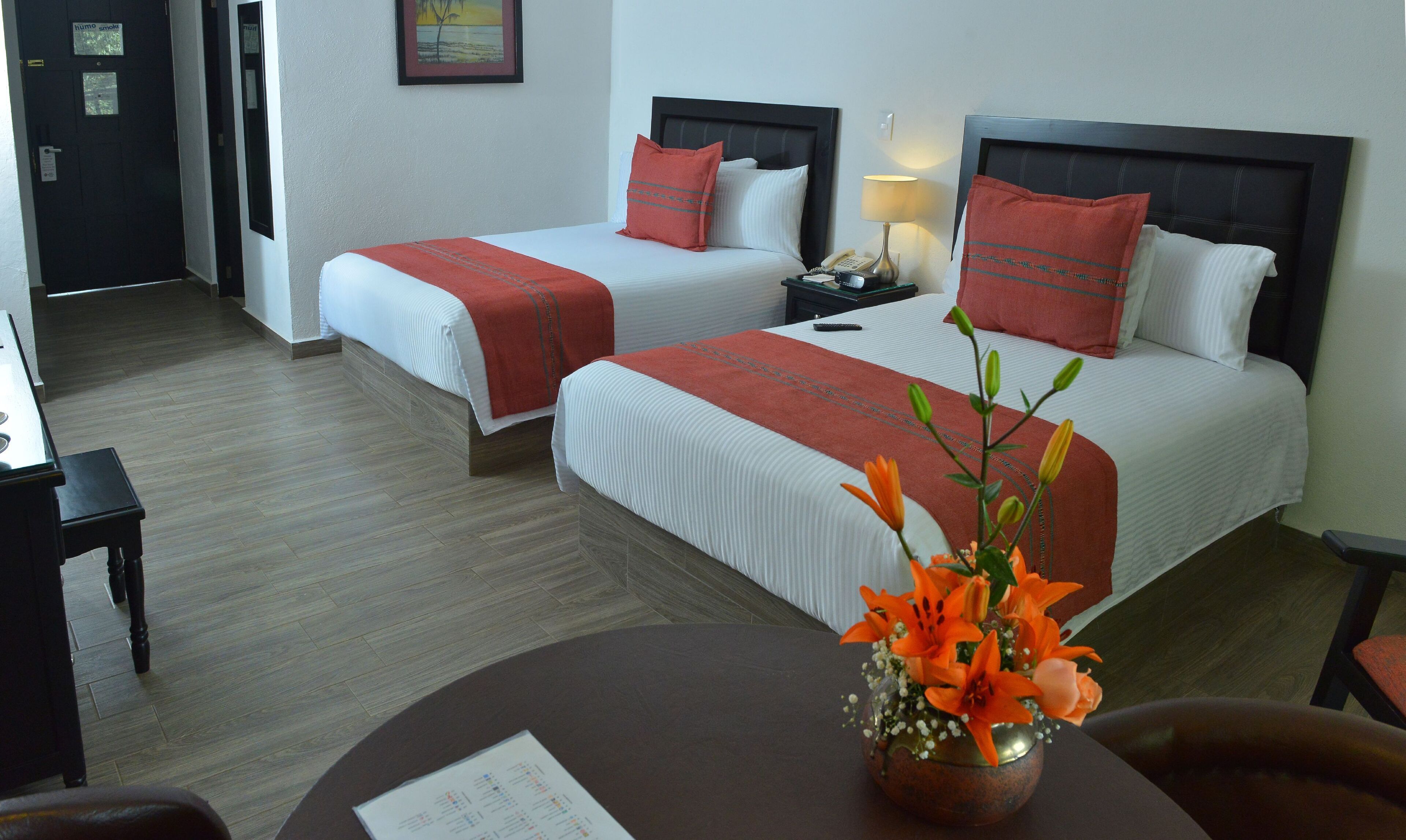 A hotel room with two beds, a desk, and a chair. There is a vase with flowers on the desk.