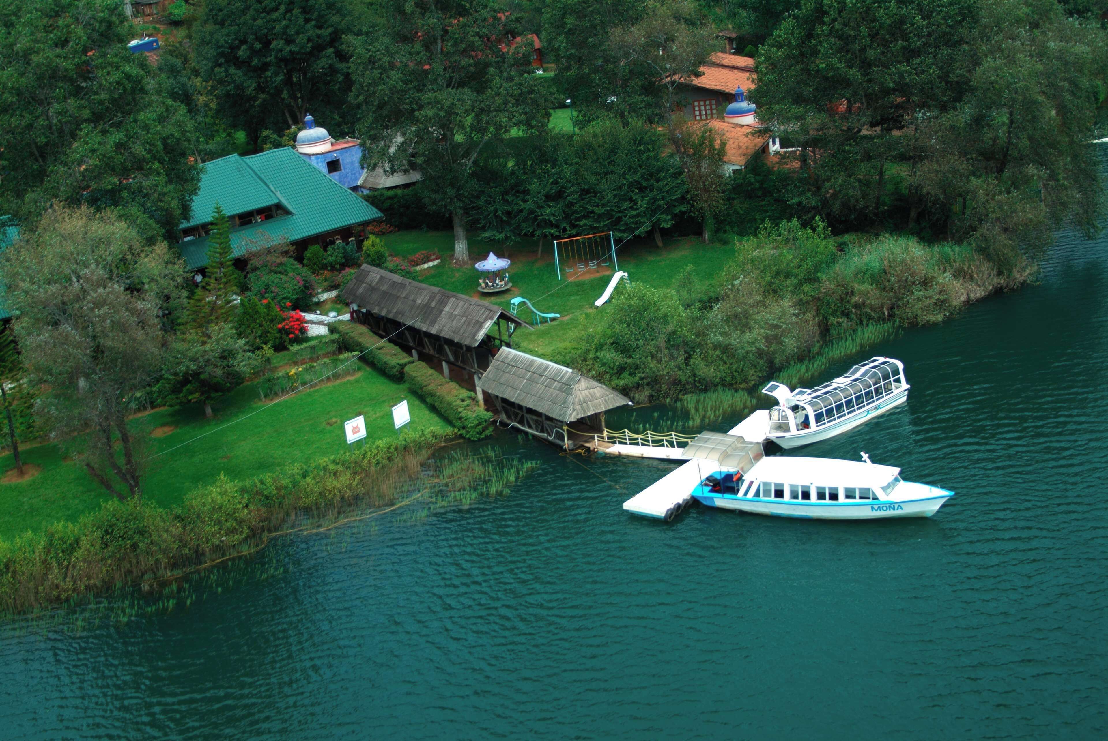 An aerial view of a lakeside property with a boat dock, a gazebo, and a house with a green roof.