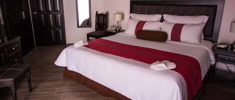 A neatly made bed with a red and white bedspread, a wooden nightstand with a lamp, and a dark wooden wardrobe.