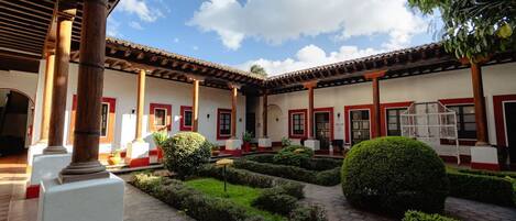 A courtyard with a tiled floor, surrounded by buildings with red-framed windows and a covered area with wooden beams.