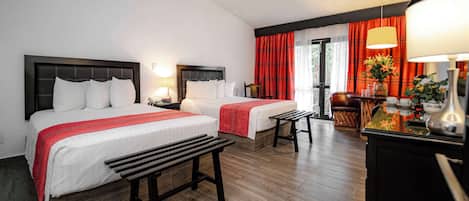 Habitación de hotel con dos camas, un banco, un escritorio con lámpara y una ventana con cortinas.
