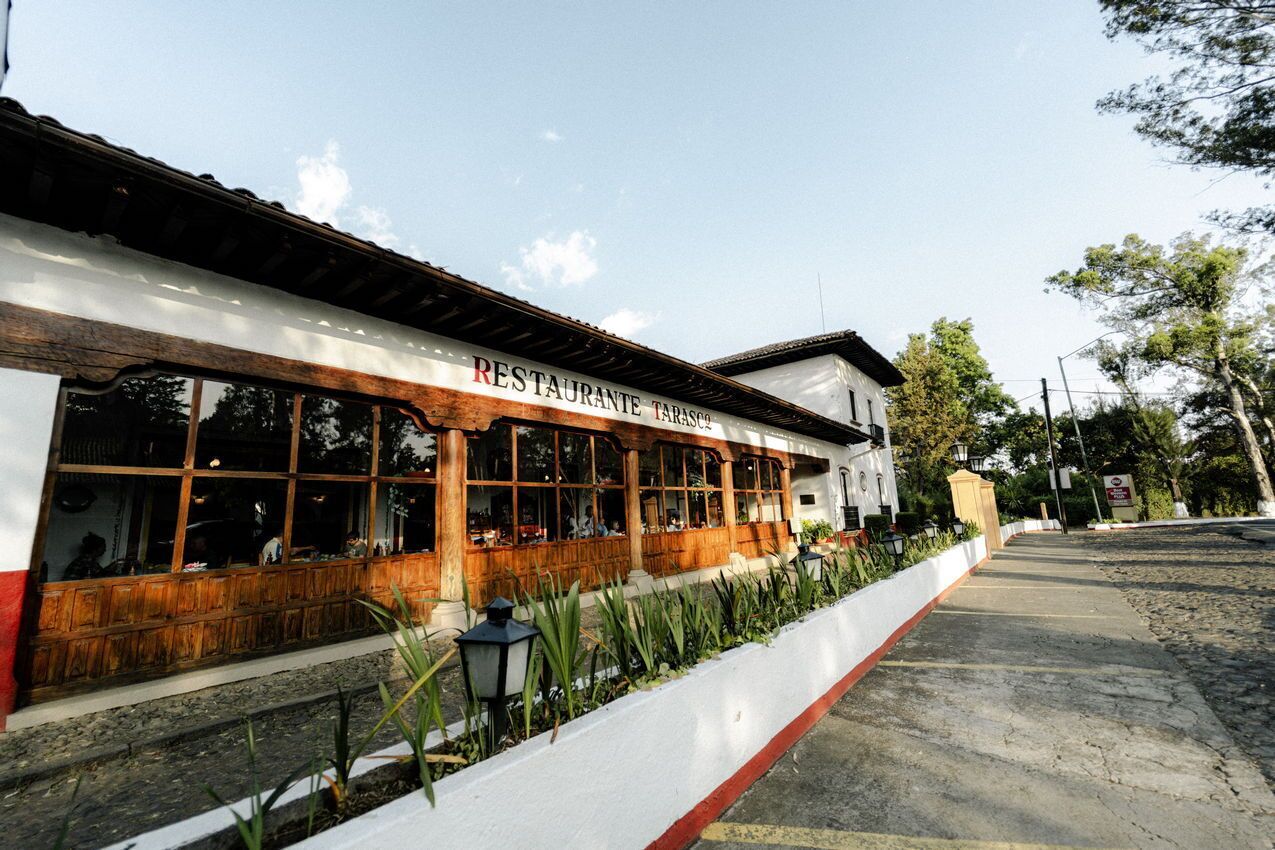 Restaurante con fachada blanca y ventanas de madera, situado junto a una acera y una calle.