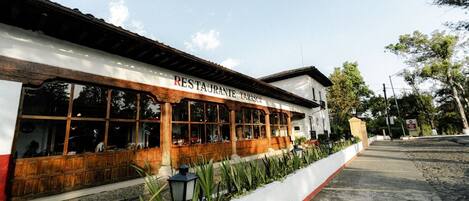 Restaurante con fachada blanca y ventanas de madera, situado junto a una acera y una calle.