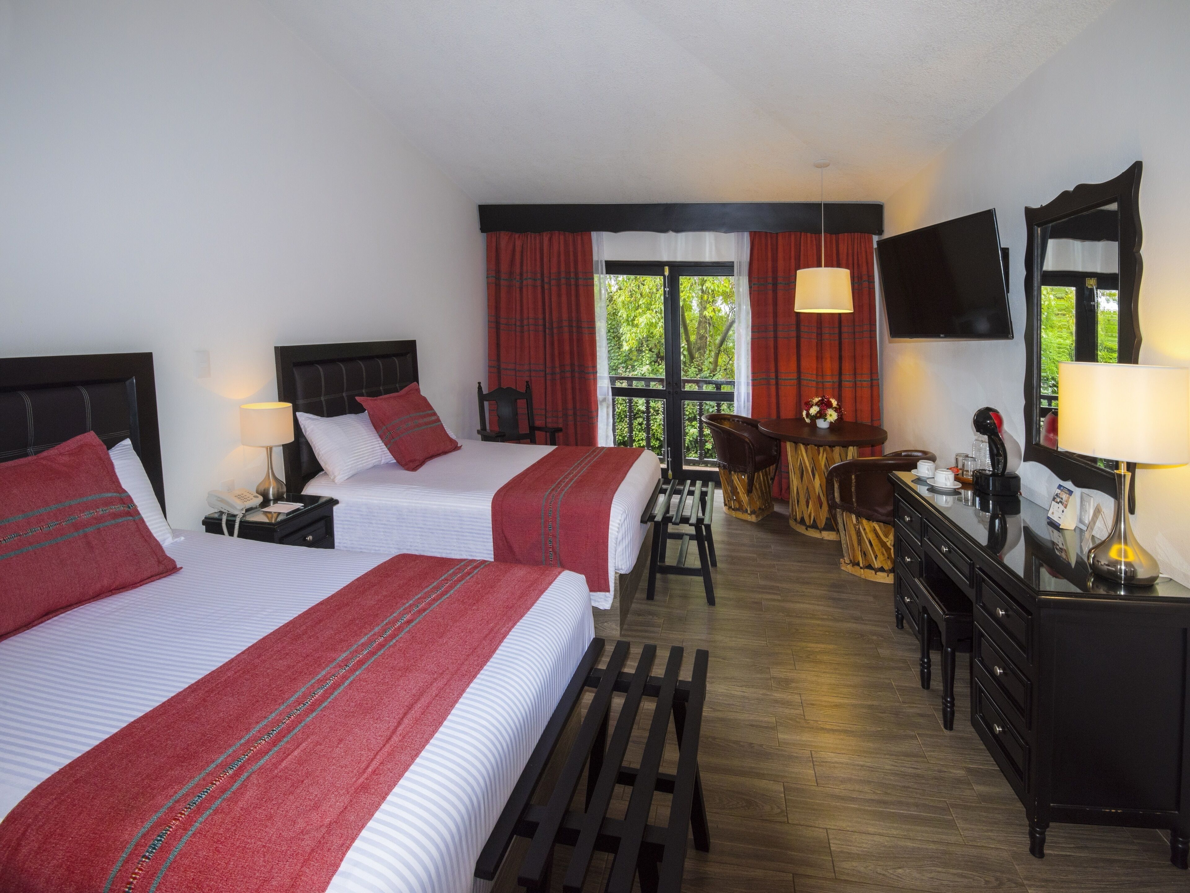 Habitación de hotel con dos camas, un escritorio con sillas, un espejo y una ventana con cortinas.