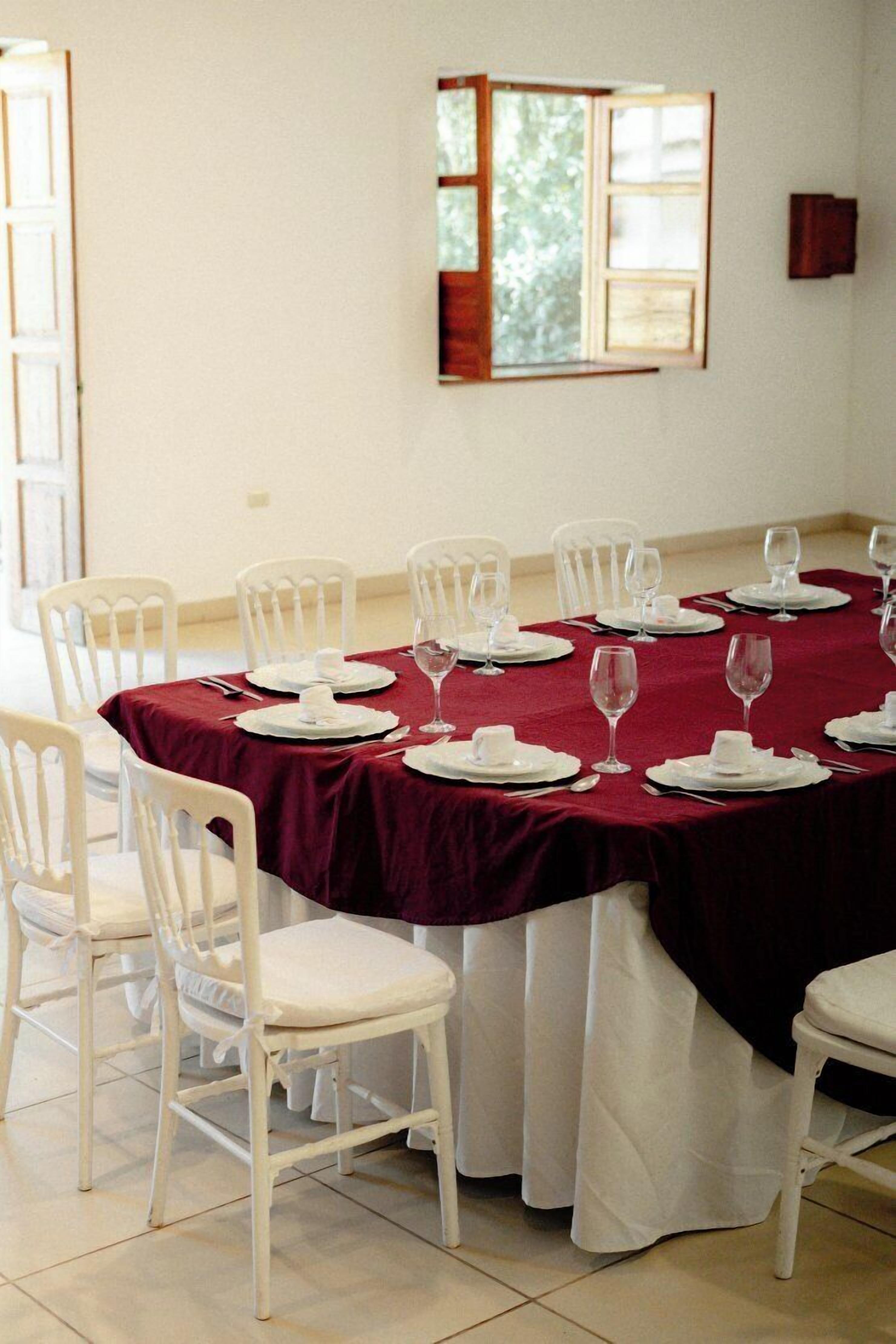 A dining room with a table set for six, white chairs, and a red tablecloth.