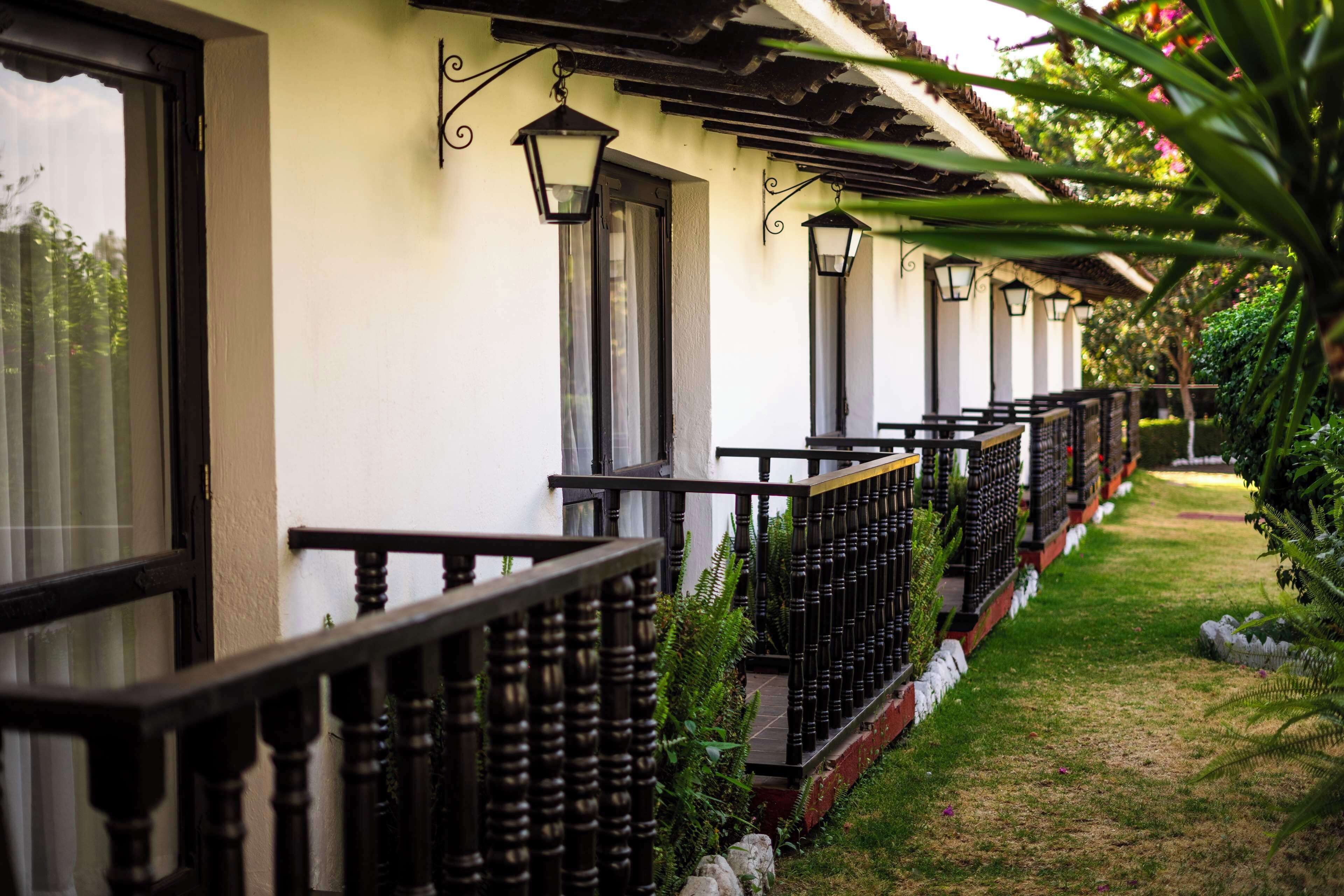 A row of white buildings with black railings and hanging lanterns, surrounded by a well-maintained garden.
