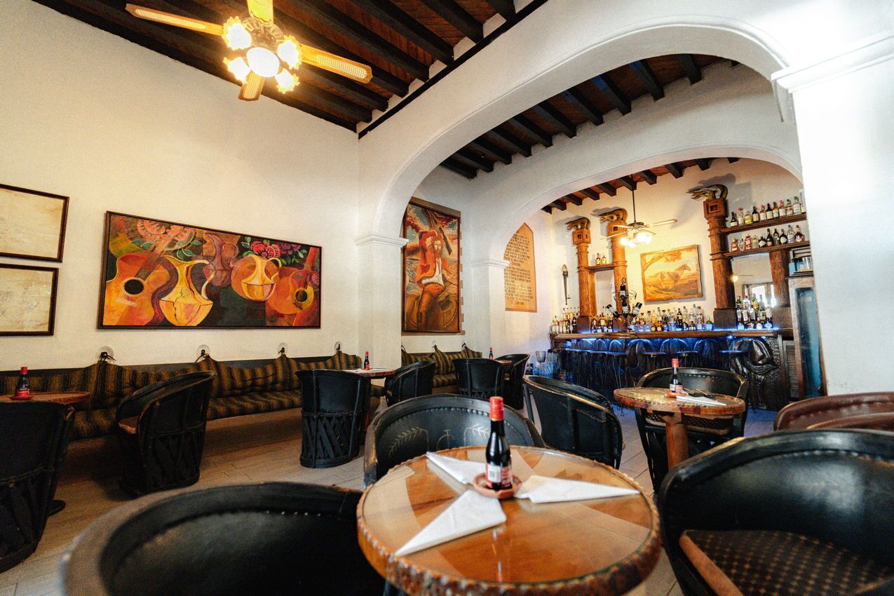 A restaurant with a bar area, wooden ceiling beams, and artwork on the walls.