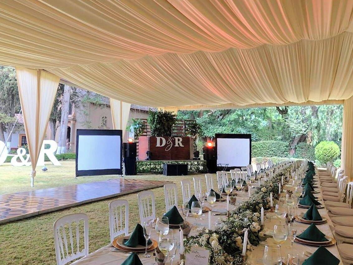 Un salón de banquetes al aire libre con una larga mesa de comedor dispuesta para un evento formal, cubierto con tela blanca.