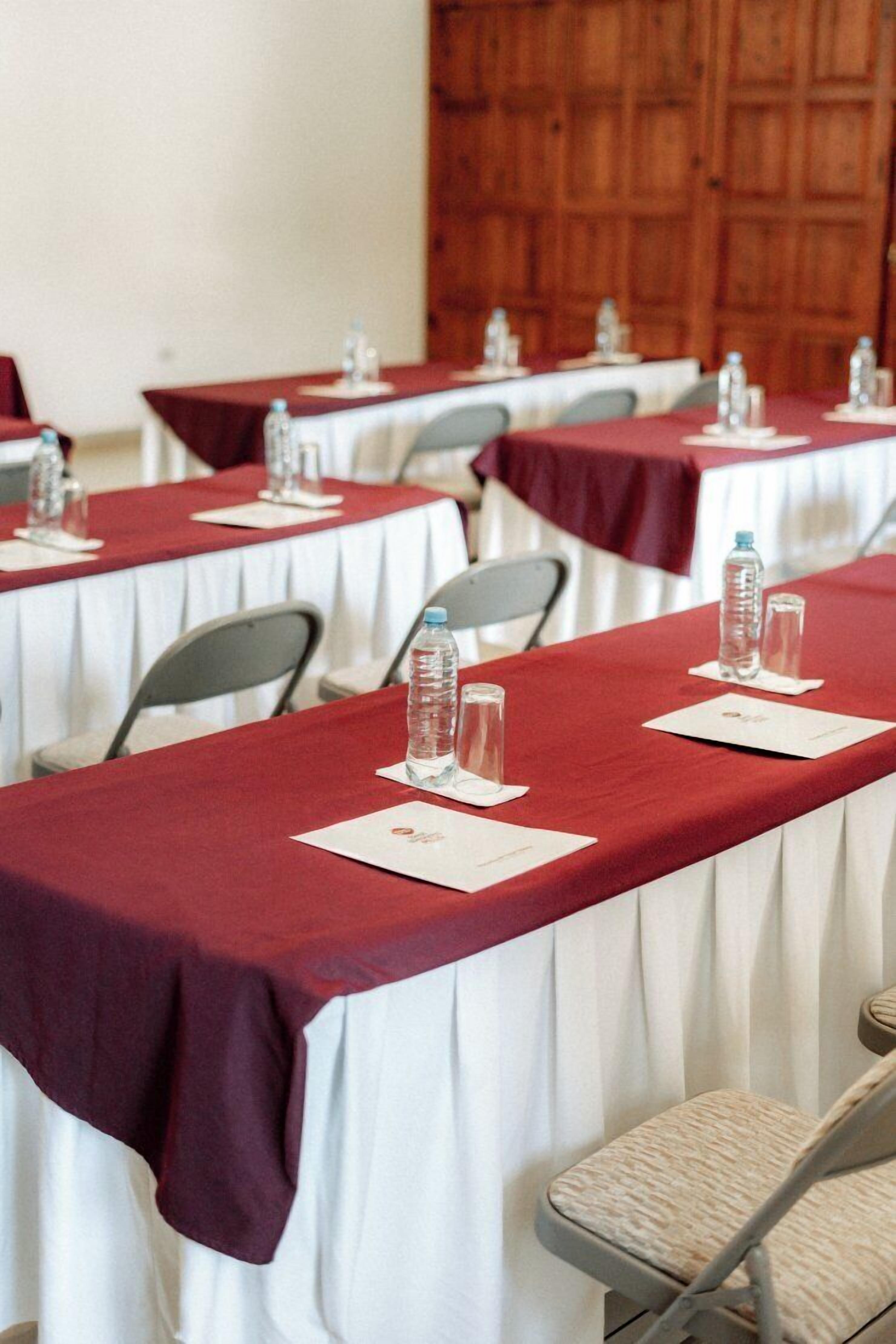 Un salón de conferencias con mesas cubiertas de manteles rojos, sillas y botellas de agua.