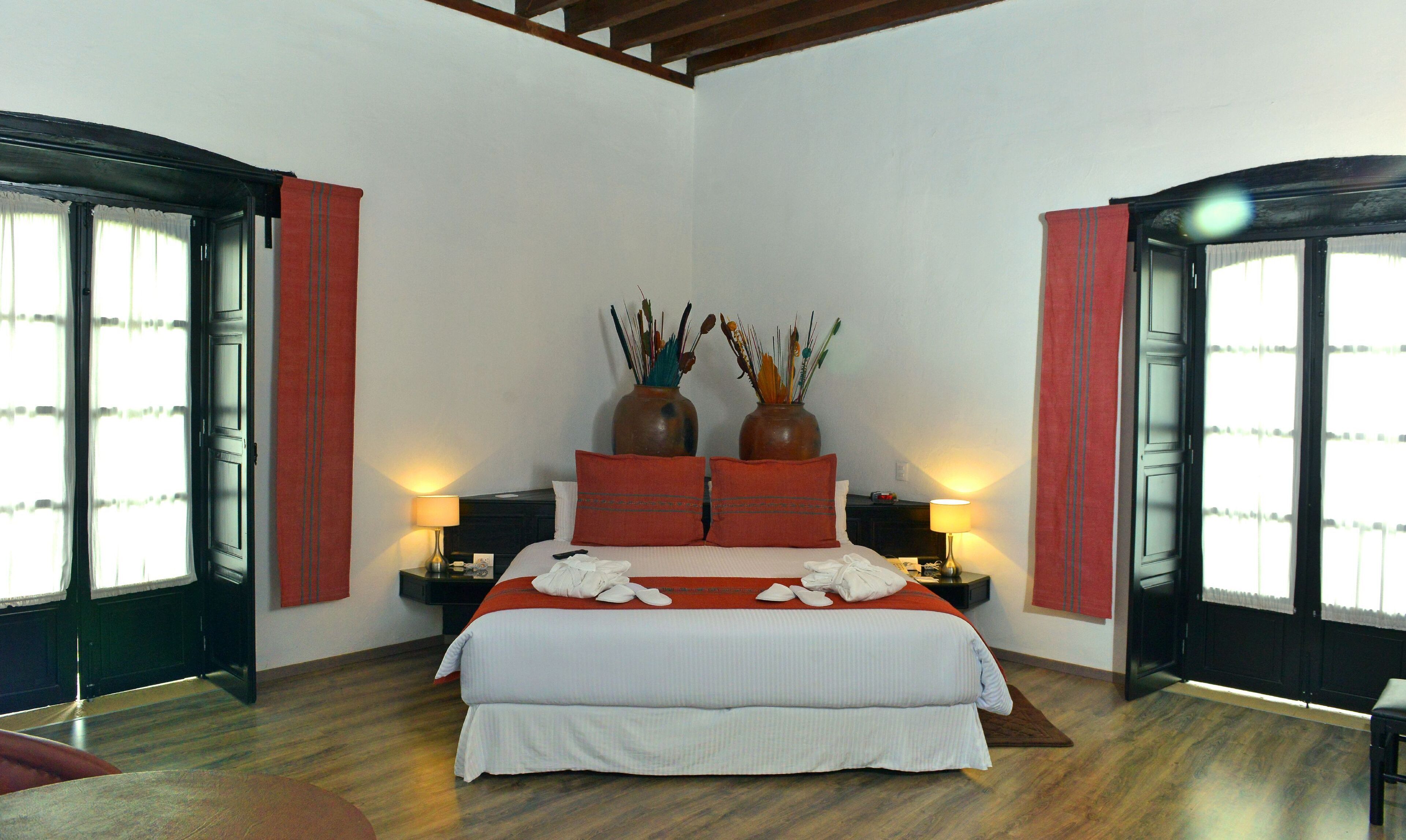 Un dormitorio con una cama grande, dos mesitas de noche, dos lámparas y dos jarrones en la cabecera.