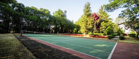 An outdoor tennis court surrounded by trees and a building.
