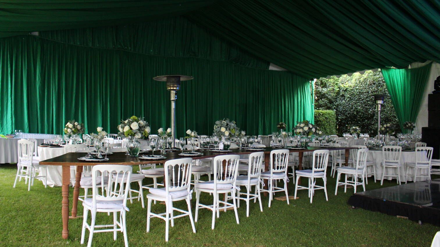 A tented outdoor dining area with white chairs and tables set up for a formal event.