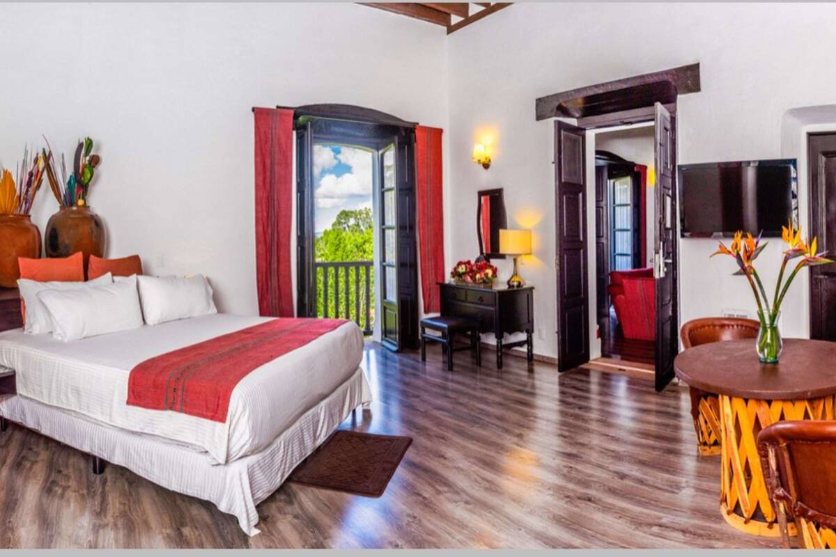 Ein Hotelzimmer mit Bett, Schreibtisch, Stuhl, Tisch und einer Tür, die auf einen Balkon führt.