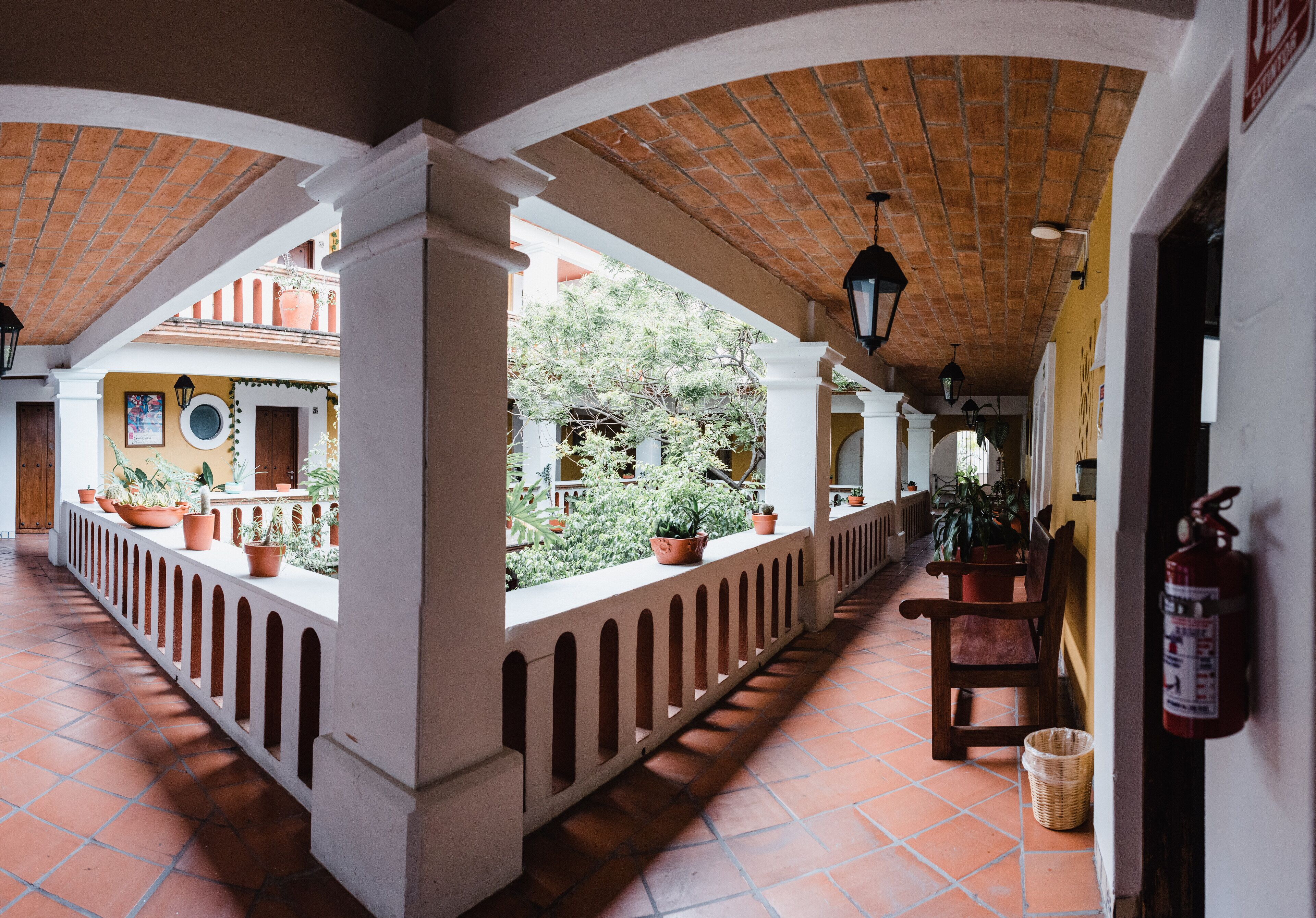 A covered outdoor corridor with terracotta tiled flooring, white columns, and potted plants.
