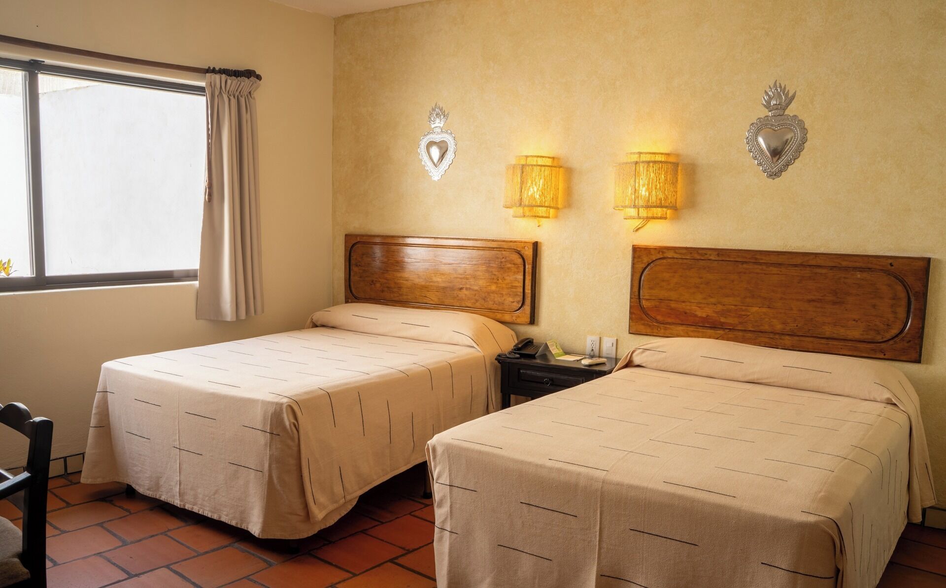 A hotel room with two beds, a nightstand, a lamp, and a window with curtains.