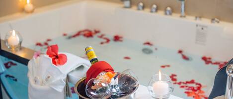 A bathtub with rose petals, a champagne bottle, and glasses.
