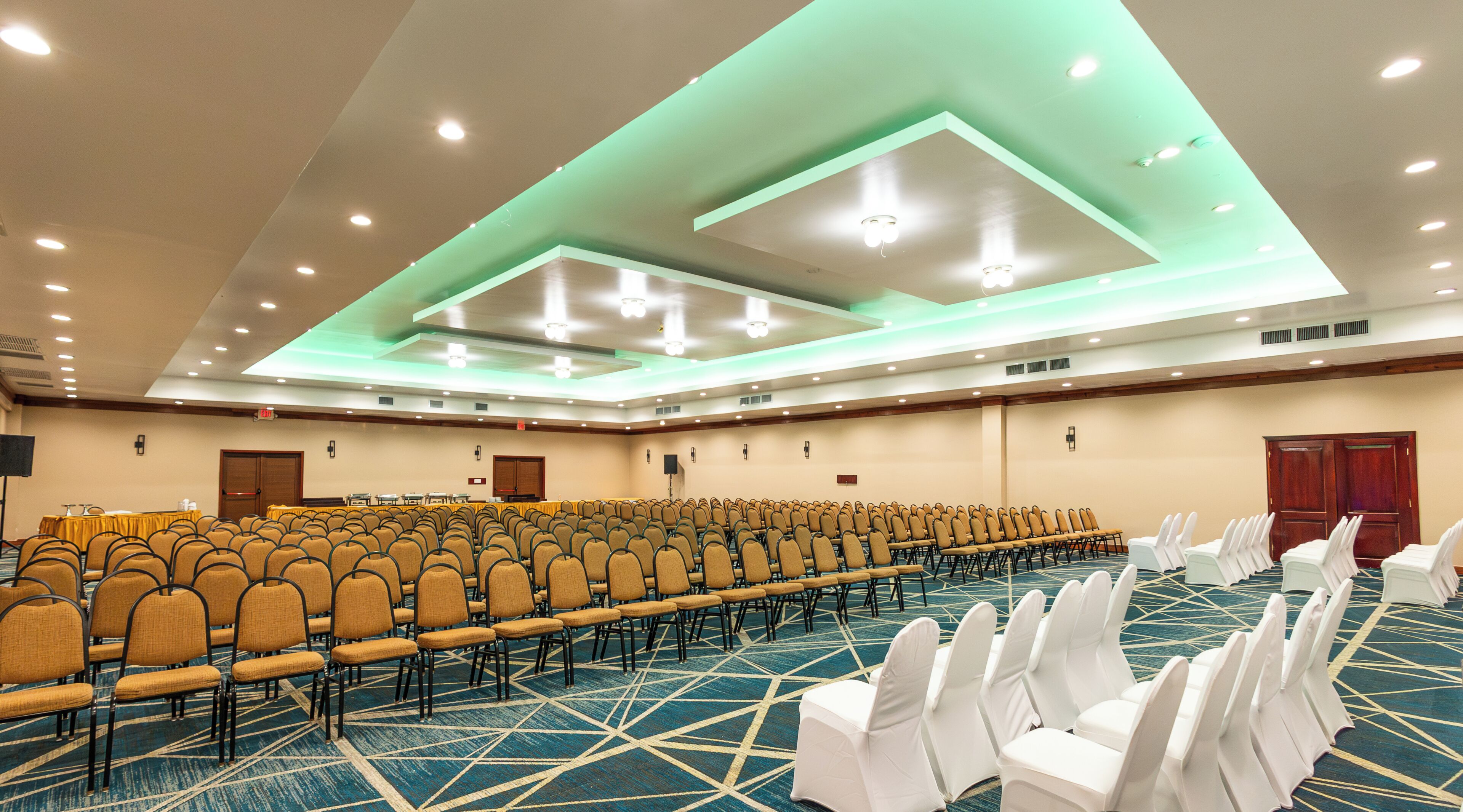 A conference room with rows of chairs, a stage, and a carpeted floor.