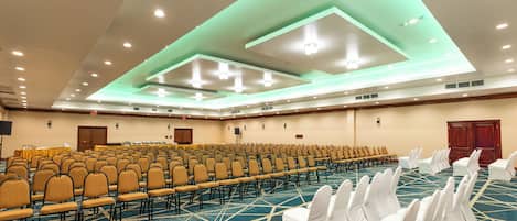 A conference room with rows of chairs, a stage, and a carpeted floor.