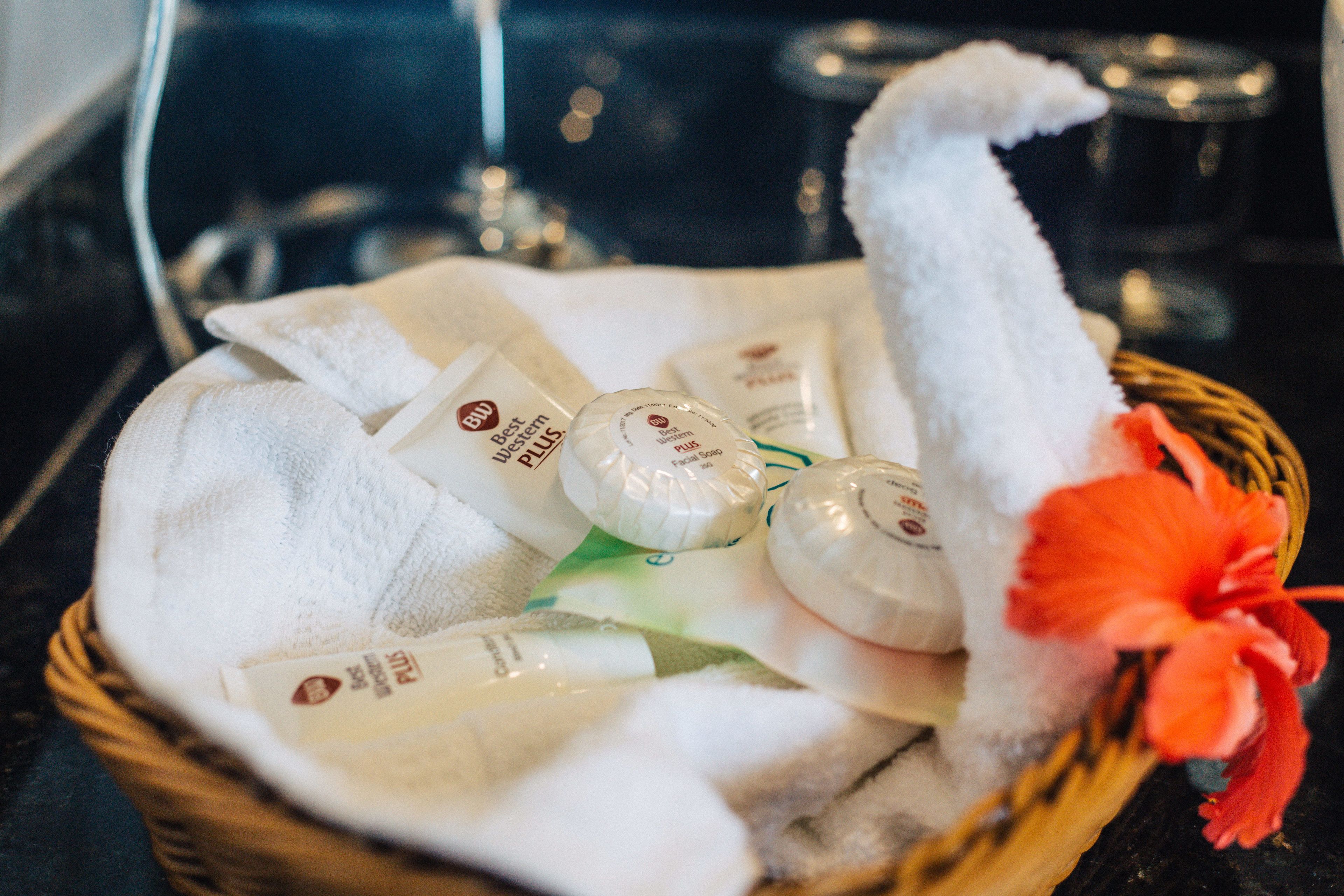 A basket containing toiletries and a white towel, with a red hibiscus flower.