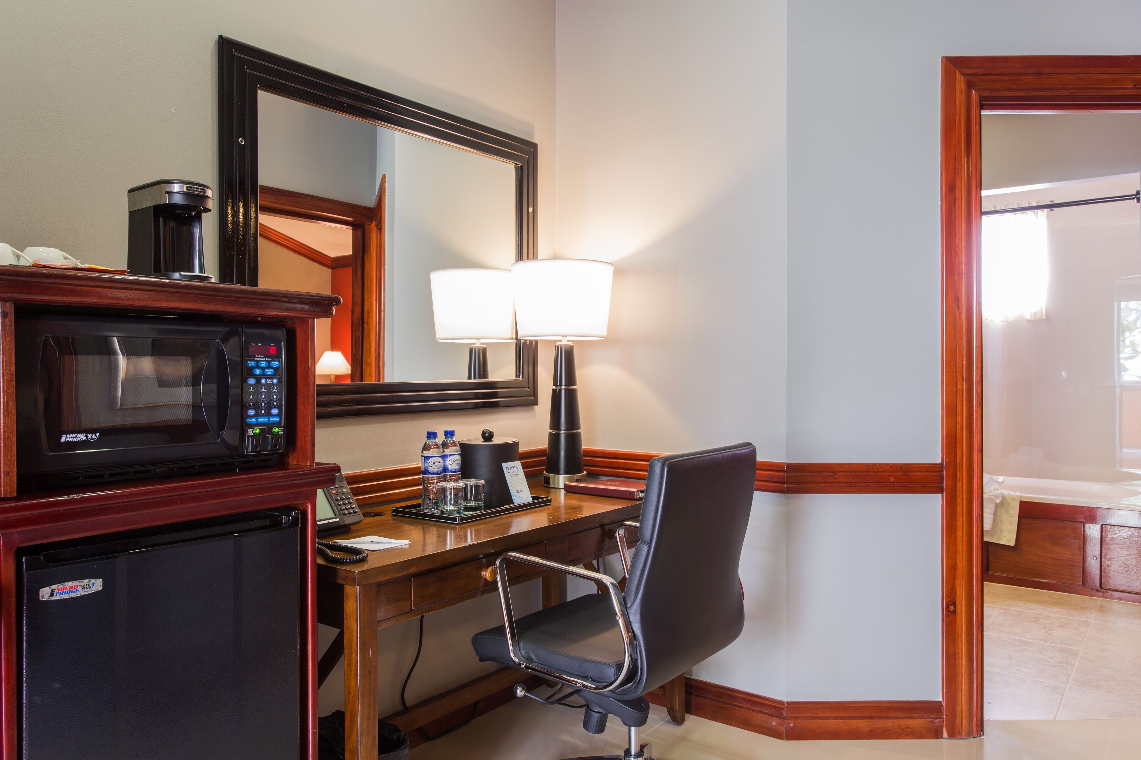 Una habitación de hotel con kitchenette, un escritorio con silla, una lámpara y un espejo.