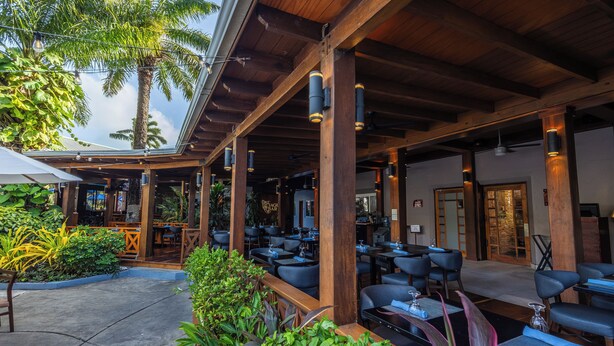 Un espace extérieur aménagé en terrasse, avec des poutres en bois, des tables et des chaises, le tout entouré de verdure.