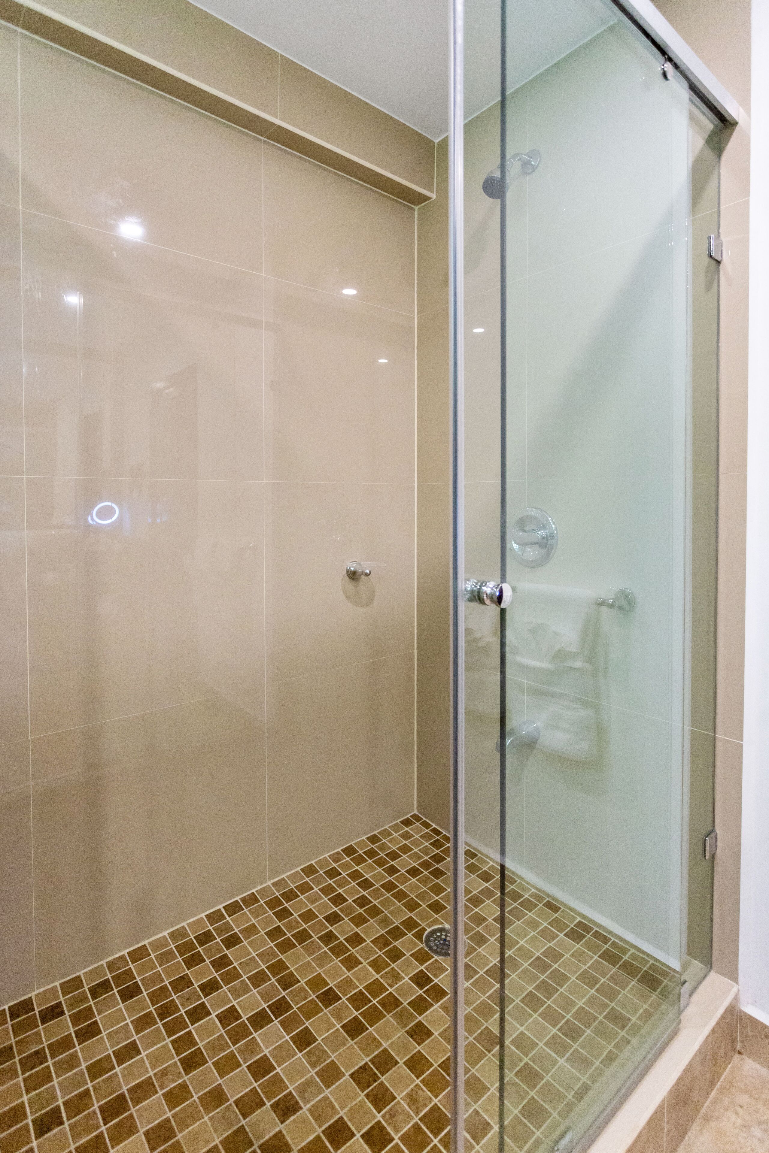 Ducha con paredes de vidrio, azulejos color beige y piso estampado.