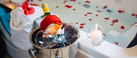 A bathtub filled with rose petals and a bottle of champagne in a bucket.
