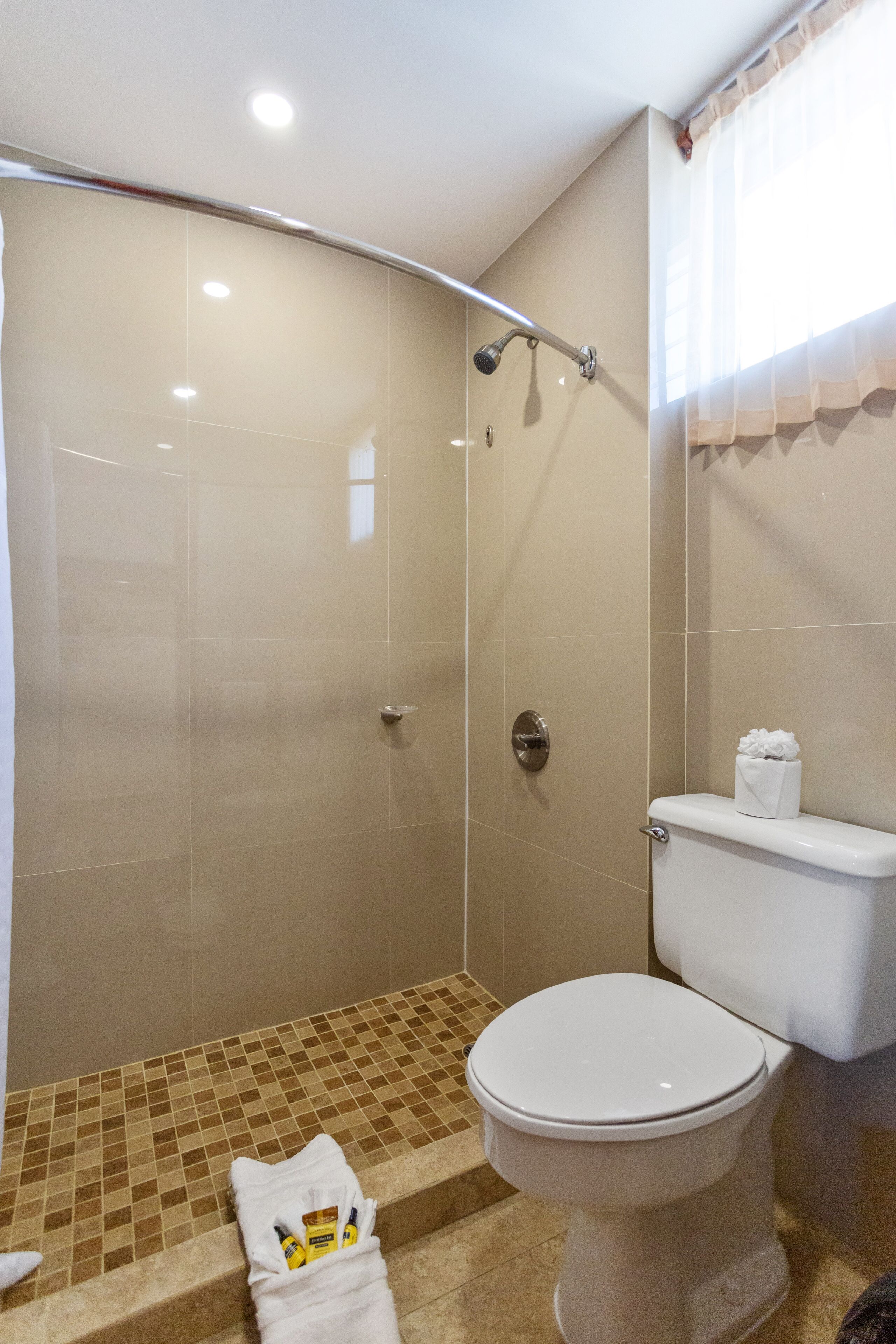 A bathroom with a shower, toilet, and a towel with toiletries on the floor.