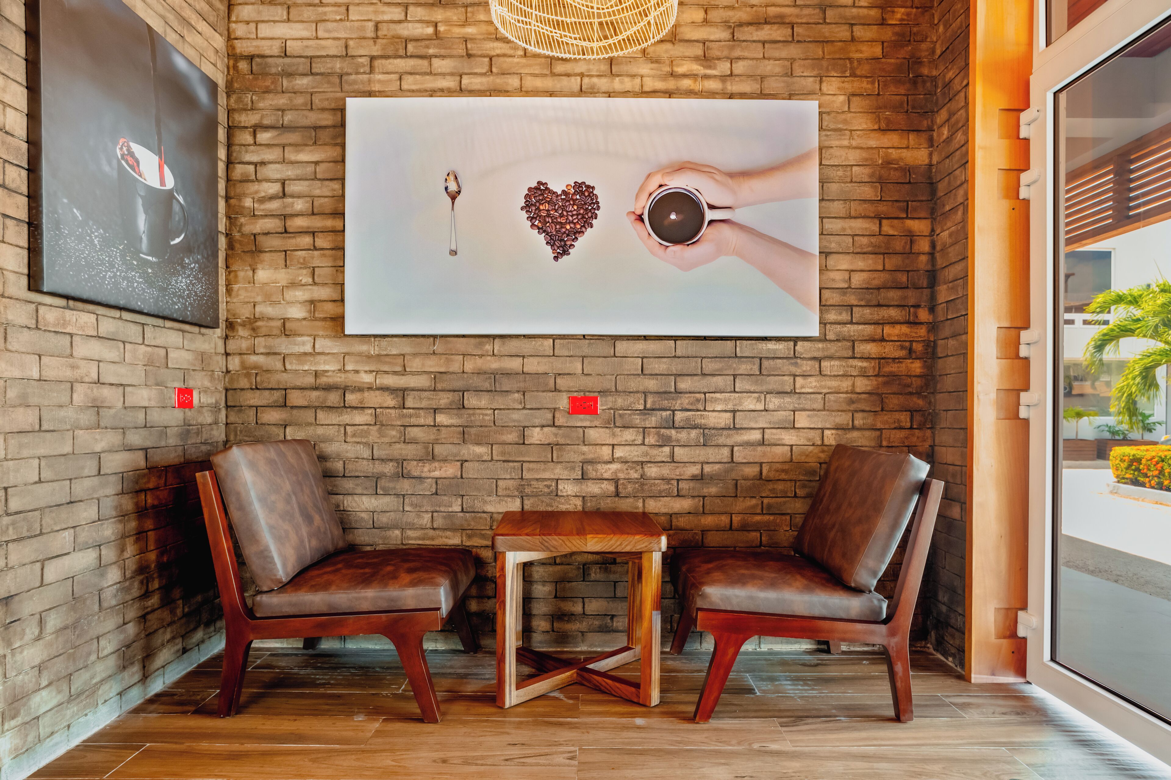 A brick wall with a painting of a hand holding a key and a heart made of coffee beans, two leather chairs, and a small wooden table.