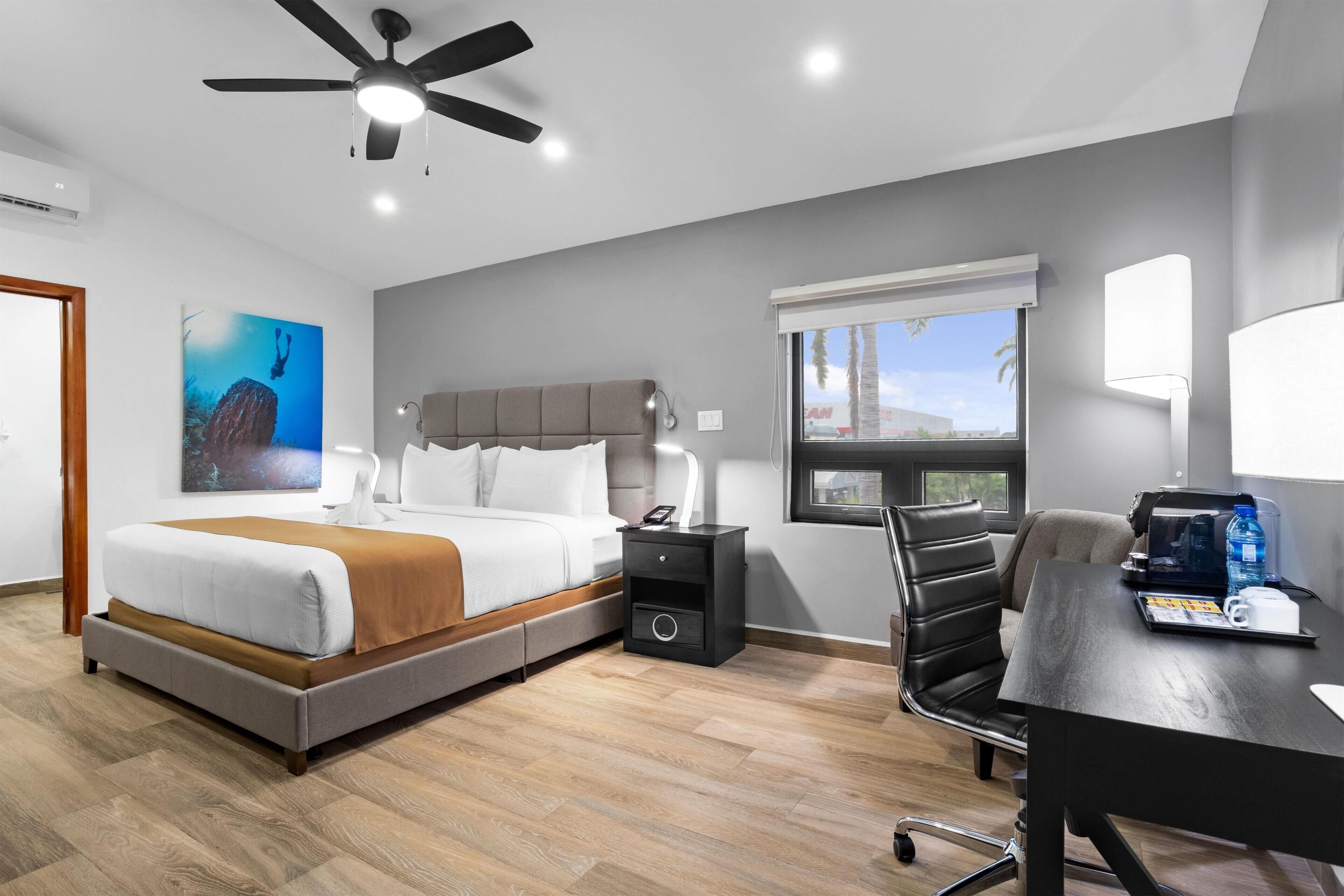 Una habitación de hotel moderna con cama, escritorio, silla, ventilador de techo y ventana con vistas.