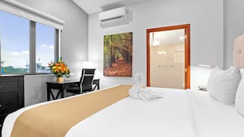 Habitación de hotel con una cama grande, un escritorio con silla, una ventana con vistas y una puerta que da a otra habitación.