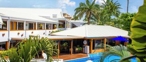 A resort with a swimming pool, covered outdoor seating, and palm trees.
